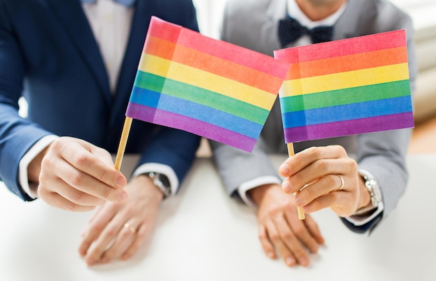 Zdjęcie ludzie, homoseksualizm, małżeństwo osób tej samej płci i koncepcja miłości - zbliżenie szczęśliwej męskiej pary gejów w garniturach i muszkach z obrączkami trzymającymi tęczowe flagi
