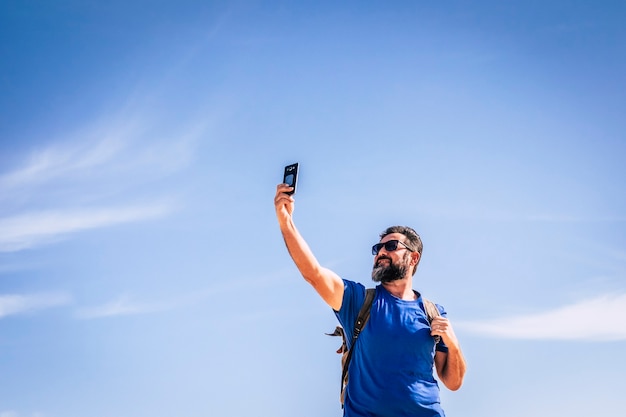 Ludzie i człowiek technologii internetowej z brodą i okularami przeciwsłonecznymi szukający sygnału za pomocą telefonu komórkowego ludzie podróżujący z plecakiem w poszukiwaniu koncepcji przygody i alternatywnych wakacji błękitne niebo