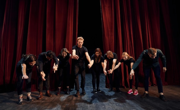 Zdjęcie ludzie kłaniający się publiczności grupa aktorów w ciemnych ubraniach na próbie w teatrze