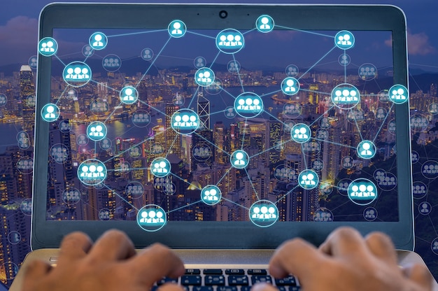 Ludzie korzystający z laptopa do łączenia się z inną osobą za pomocą diagramu sieci bezprzewodowej nad miastem w nocy, które reprezentują komunikację internetową w świecie.