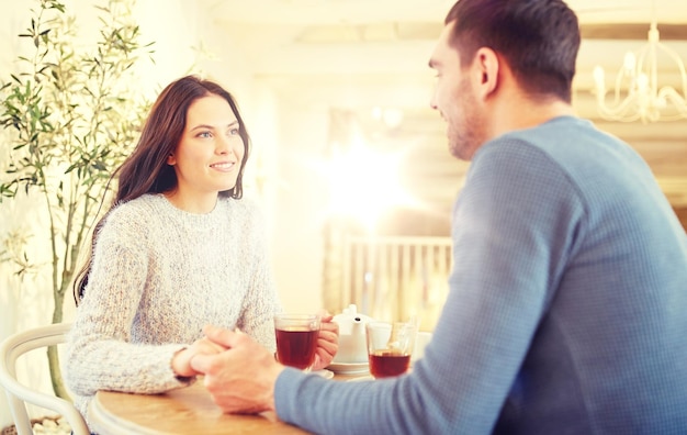 ludzie, miłość, romans i randki koncepcja - szczęśliwa para pijąca herbatę i trzymająca się za ręce w kawiarni lub restauracji