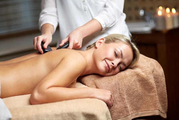 ludzie, piękno, spa, zdrowy styl życia i koncepcja relaksu - zbliżenie pięknej młodej kobiety podczas masażu gorącymi kamieniami w spa