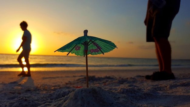 Ludzie piją parasole na plaży na tle nieba podczas zachodu słońca