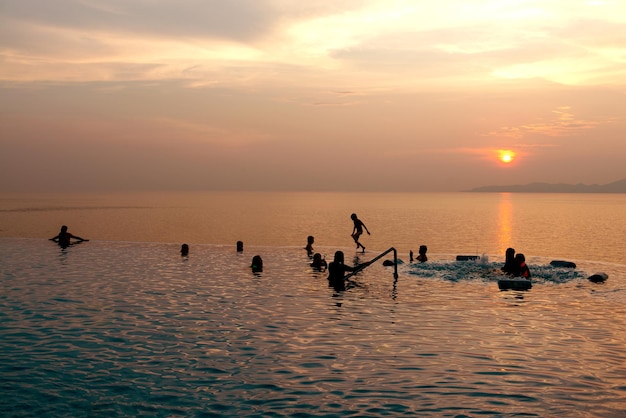 Ludzie pływający, bawiący się w basenie - Młodzi ludzie cieszą się wakacjami w tropikalnym hotelu wypoczynkowym i pięknym zachodem słońca nad morzem o zmierzchu - Vintage Filter