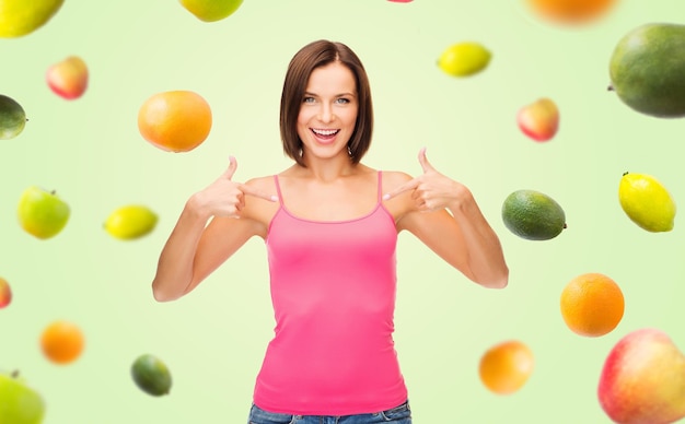 ludzie, reklama, dieta, jedzenie i koncepcja zdrowego odżywiania - uśmiechnięta kobieta w pustym różowym podkoszulku wskazując palcami do siebie nad owocami na zielonym tle