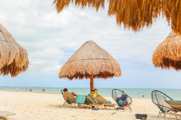 Ludzie relaksujący się na plaży przed krytym strzechą parasolem