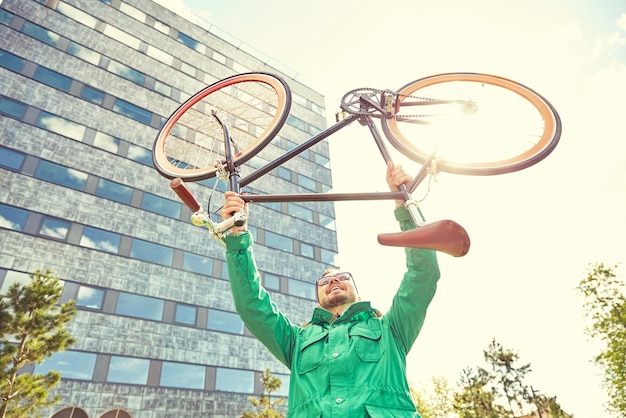 Zdjęcie ludzie, sport, styl, wypoczynek i styl życia - szczęśliwy młody hipster mężczyzna wstający i trzymający rower z ostrym kołem w mieście