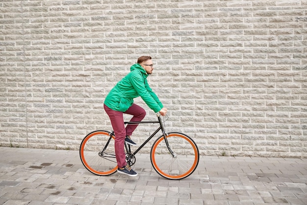 ludzie, styl, wypoczynek i styl życia - młody hipster mężczyzna jedzie na rowerze stacjonarnym na ulicy miasta na tle ceglanego muru