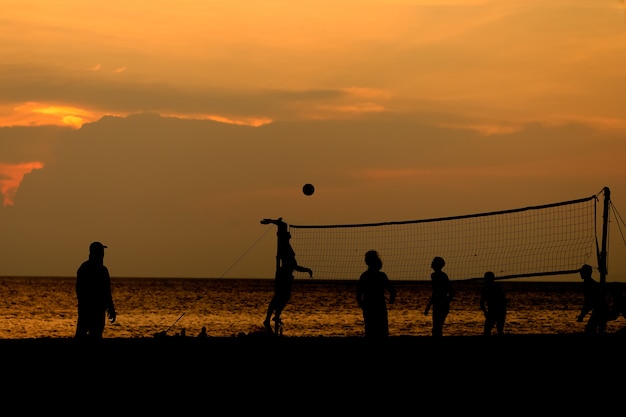 Ludzie sylwetki grają w siatkówkę plażową.