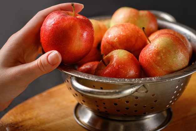 Ludzka ręka bierze jedno jabłko z metalowej miski pełnej czerwonych dojrzałych jabłek. Zdrowe odżywianie. Składniki szarlotki. Gotowanie w domu