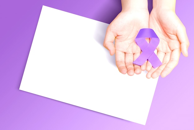 Ludzką ręką pokazano fioletowe wstążki z pustym białym papierem na kolorowym tle. Światowy dzień walki z rakiem. Pusty biały papier do miejsca na kopię