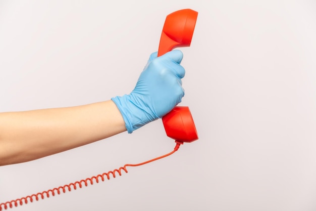 Ludzka ręka w niebieskich rękawiczkach chirurgicznych, trzymając i pokazując słuchawkę słuchawki telefonicznej w kolorze czerwonym.