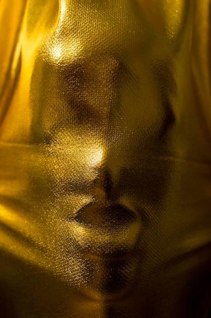 Ludzka twarz naciskająca złotą tkaninę