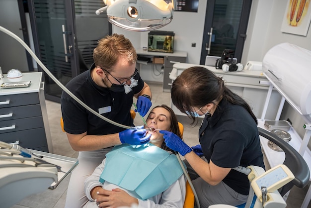 Zdjęcie ludzki dentysta operuje młodą uśmiechniętą dziewczynę w klinice dentystycznej