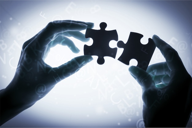 Ludzkie ręce łączące części puzzli na tle