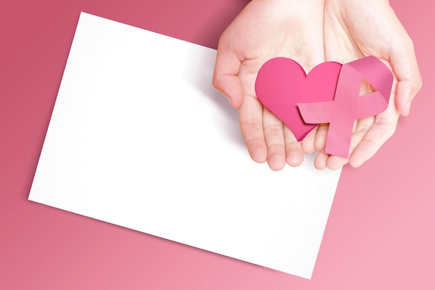 Ludzkie ręce pokazujące różową wstążkę świadomości, serce i pusty papier. Świadomość raka piersi. Pusty papier na miejsce na kopię
