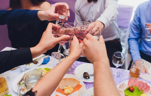 Zdjęcie ludzkie ręce z kieliszkami czerwonego wina dźwięczącymi je nad podawanym stołem