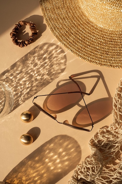 Luksusowa, artystyczna kompozycja mody estetycznej Szkło kryształowe z cieniami słońca okulary przeciwsłoneczne damski słomkowy kapelusz torebka sznurkowa złote kolczyki na neutralnym beżowym tle Płaski widok z góry