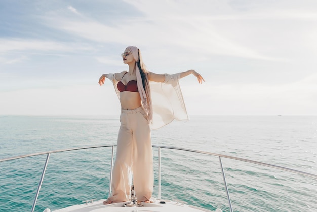Luksusowa młoda kobieta w stylowych letnich ubraniach pozuje na białej łodzi płynącej na wyspę