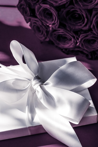Luksusowe świąteczne jedwabne pudełko i bukiet róż na fioletowym tle romantyczna niespodzianka i kwiaty jako prezent urodzinowy lub walentynkowy