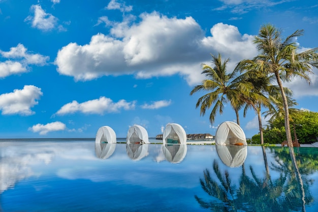 Luksusowy basen z palmami i leżakami z baldachimem plażowym. Idylliczne błękitne niebo przy basenie