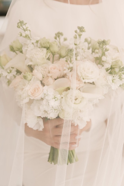 Luksusowy bukiet ślubny z białymi różami w rękach Panny Młodej pod welonem