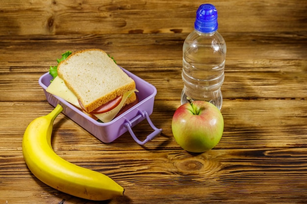 Lunch box z kanapkami butelka wody banan i jabłko na drewnianym stole