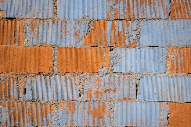 Łuszcząca się farba na ścianie z cegły w odcieniach szarości i kremu z plamami odsłoniętej cegły