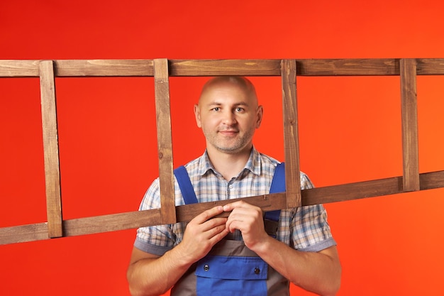 Zdjęcie Łysy mężczyzna trzyma poziomo drewnianą drabinę i patrzy przez ramę