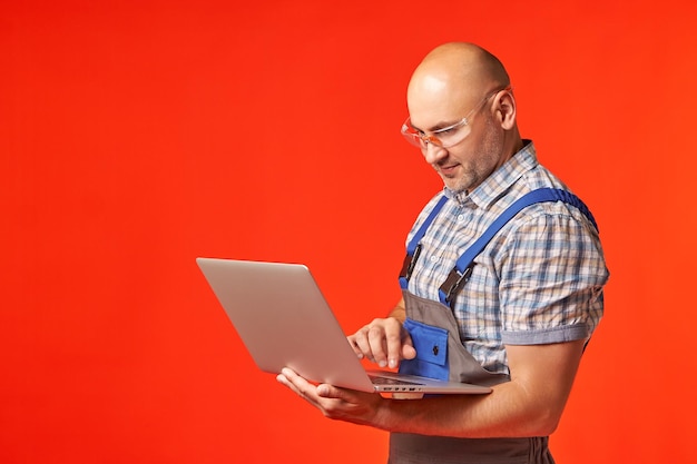 Łysy mężczyzna w okularach ochronnych trzyma w ręku i pracuje na laptopie