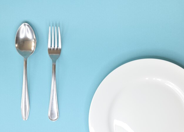 Łyżka stołowa i widelec leżący obok białego talerza na niebieskim tle