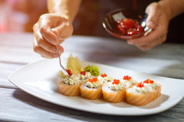 Łyżka z kawiorem na sushi. Ręka mężczyzny trzymająca małą łyżeczkę. Serek i kawior z łososia. Najlepszy przepis na bułeczki uramaki.