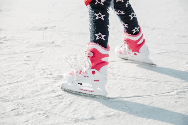Zdjęcie Łyżwy figurowe na dziewczęcych nogach na lodzie pokrytym śniegiem i śladami jazdy na łyżwach. dziecko zima na zewnątrz na lodowisku. lód i nogi