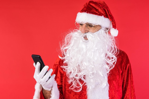 M??czyzna ubrany jak Santa Claus konsultacji jego telefon komórkowy na czerwonym tle Bo?e Narodzenie celebracja prezenty konsumpcjonizmu i koncepcji szcz??cia