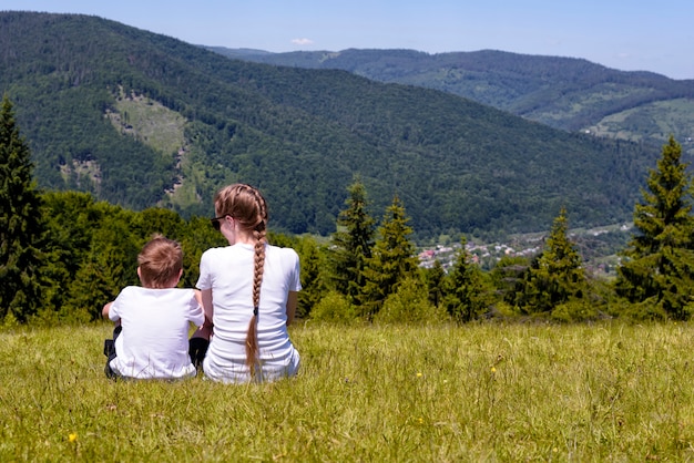 Macierzysty i młody syna obsiadanie na trawie dalej iglasty las i góry