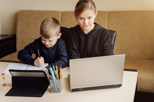 Macierzysty używa laptopu i pastylki nauczanie z jej synem online w domu w jego pokoju