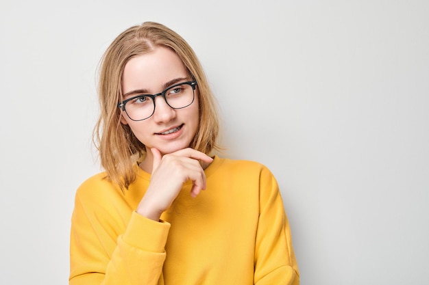 Mądra blond studentka z okularami dotyka podbródka myśli wybiera odizolowane na białym tle studia z przestrzenią kopiowania pewność siebie inteligentny geniusz