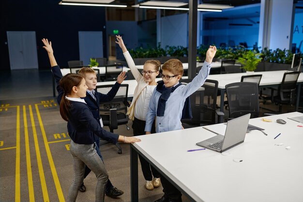Zdjęcie mądre dzieci podniosły rękę świętują sukces. zespół biznesowy małych dzieci pokazujący zwycięski gest