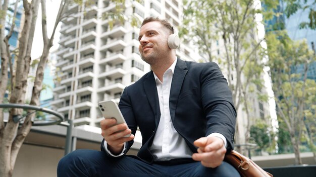 Mądrzy biznesmeni noszą słuchawki podczas oglądania telefonu w zielonym mieście Urbane