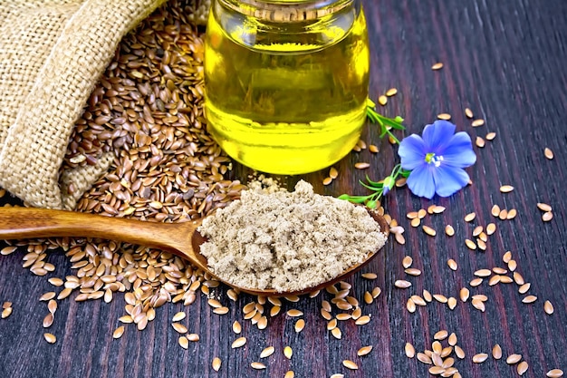 Zdjęcie mąka lniana w łyżce oleju w szklanym słoju niebieski lniany kwiat i brązowe nasiona w woreczku na drewnianej desce tle