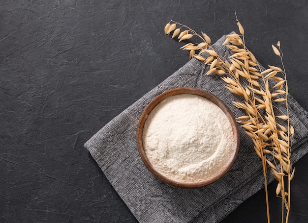 Mąka owsiana i sucha gałąź na ciemnym tle z serwetką Organiczne składniki do pieczenia Koncepcja domowego i zdrowego jedzenia