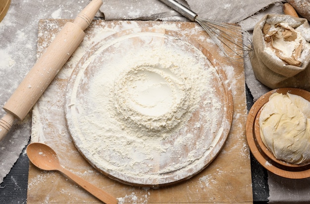 Mąka pszenna biała ułożona na okrągłej drewnianej desce, zagniecione ciasto na drewnianym talerzu, widok z góry