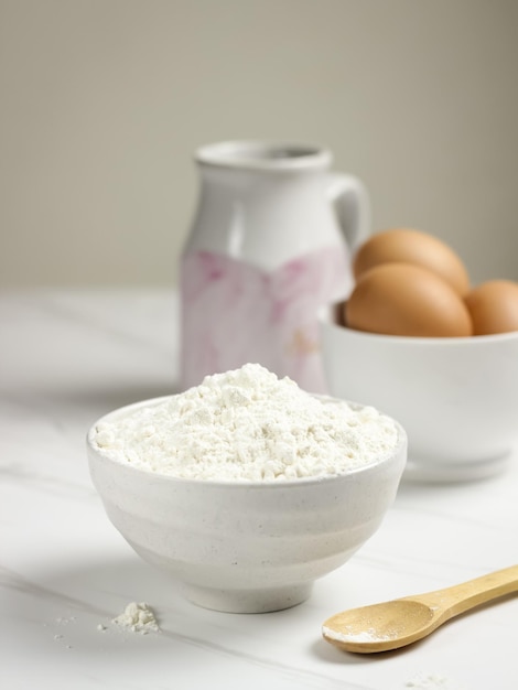 Mąka pszenna w białej misce z jajkami i mlekiem jako tło. Koncepcja przygotowania do pieczenia.