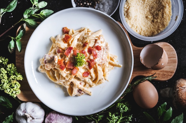 Makaron carbonara w białym naczyniu otoczony świeżym składnikiem