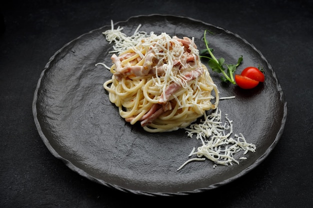 Makaron Carbonara z serem i pomidorami na czarnym talerzu