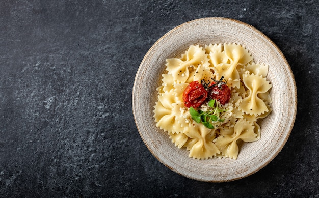 Makaron Farfalle w talerzu ceramicznym na powierzchni z ciemnego kamienia, widok z góry, miejsce na kopię