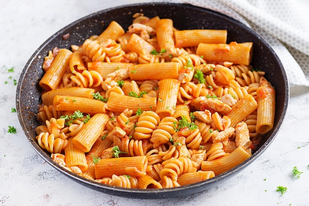 Makaron Fusilli W Sosie Pomidorowym Z Kurczakiem, Pomidory Ozdobione Natką Pietruszki Na Jasnym Stole.