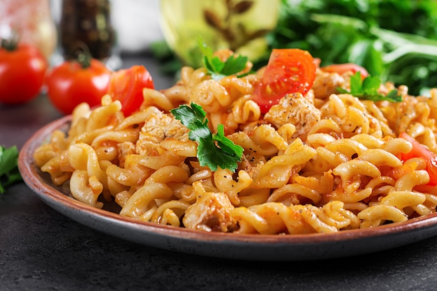 Makaron Fusilli z pomidorami, mięsem z kurczaka i natką pietruszki na talerzu na ciemnym stole.