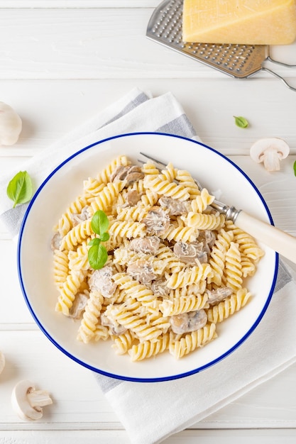 Makaron Fusilli z serem grzybowym i świeżą bazylią w talerzu na białym drewnianym tle