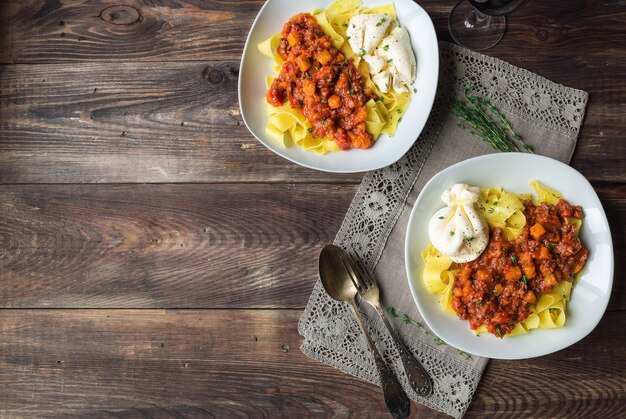 Makaron Pappardelle z ragoutem mięsnym z dynią i serem burrata na rustykalnej drewnianej powierzchni. Kuchnia włoska. Widok z góry. Skopiuj obszar przestrzeni.